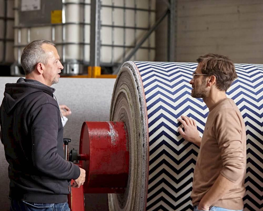 Employees of Weverij talking next to big roll of fabric